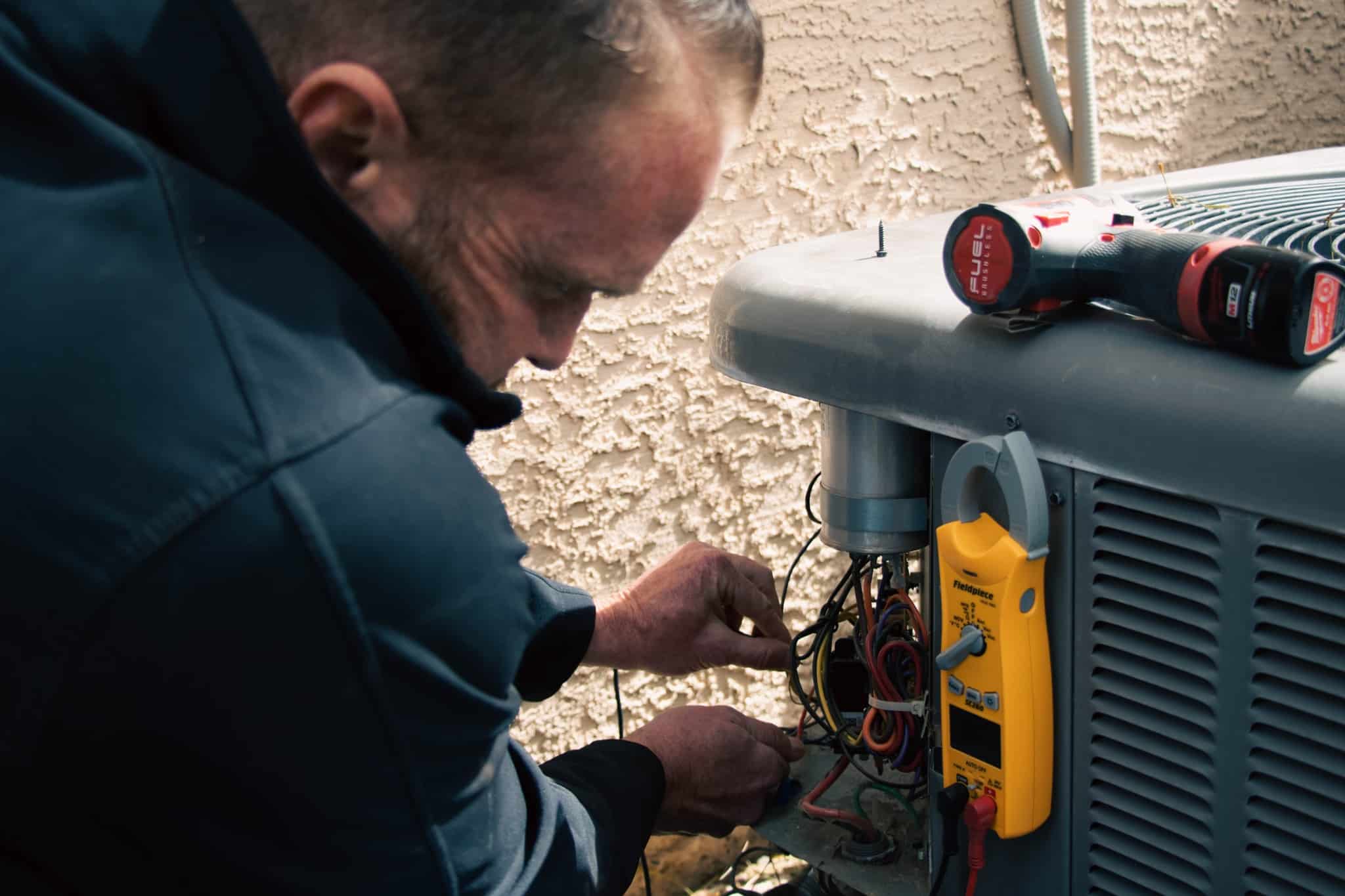 A technician repairing an HVAC unit outside a building with tools nearby.